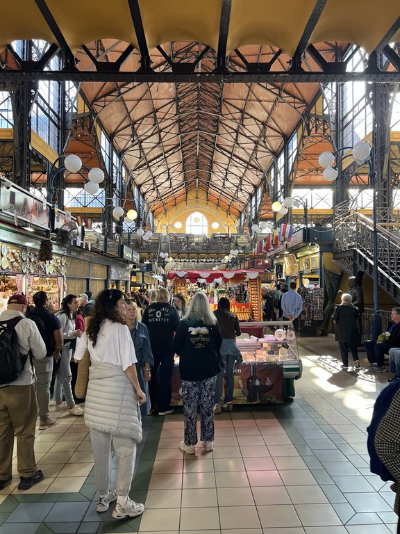 Central Market Hall içinde yüksek tavan, metal taşıyıcılar ve tezgâhlar arasındaki ziyaretçiler