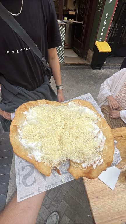 Langos Papi önünde elde tutulan geniş, peynirli klasik lángos porsiyonu