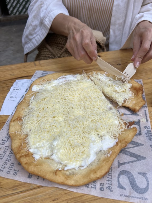 Ahşap masada peynirli ve ekşi kremalı lángosun kesilmesi